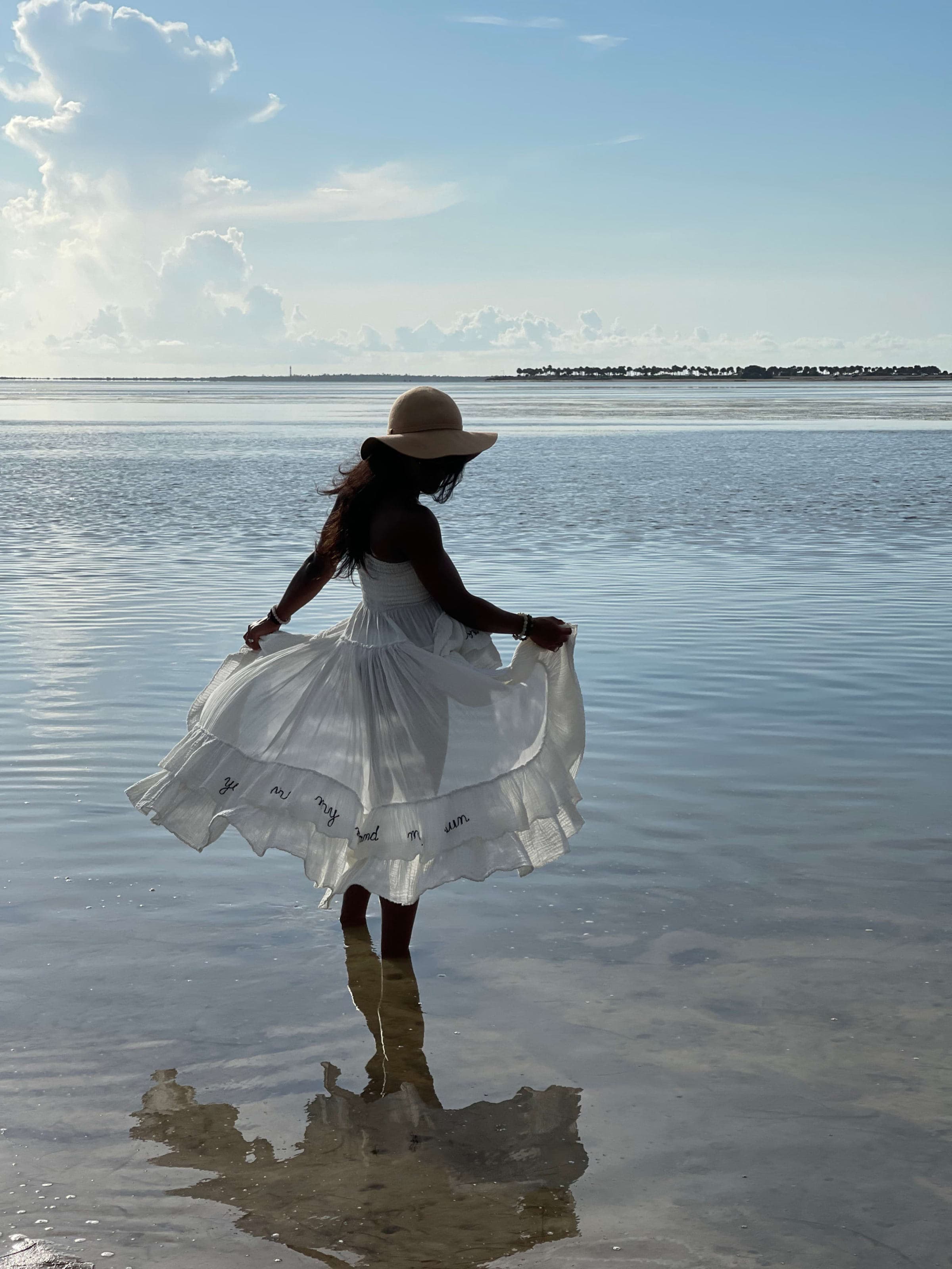Lauren Lease standing in shallow water in a white dress, looking out to sea